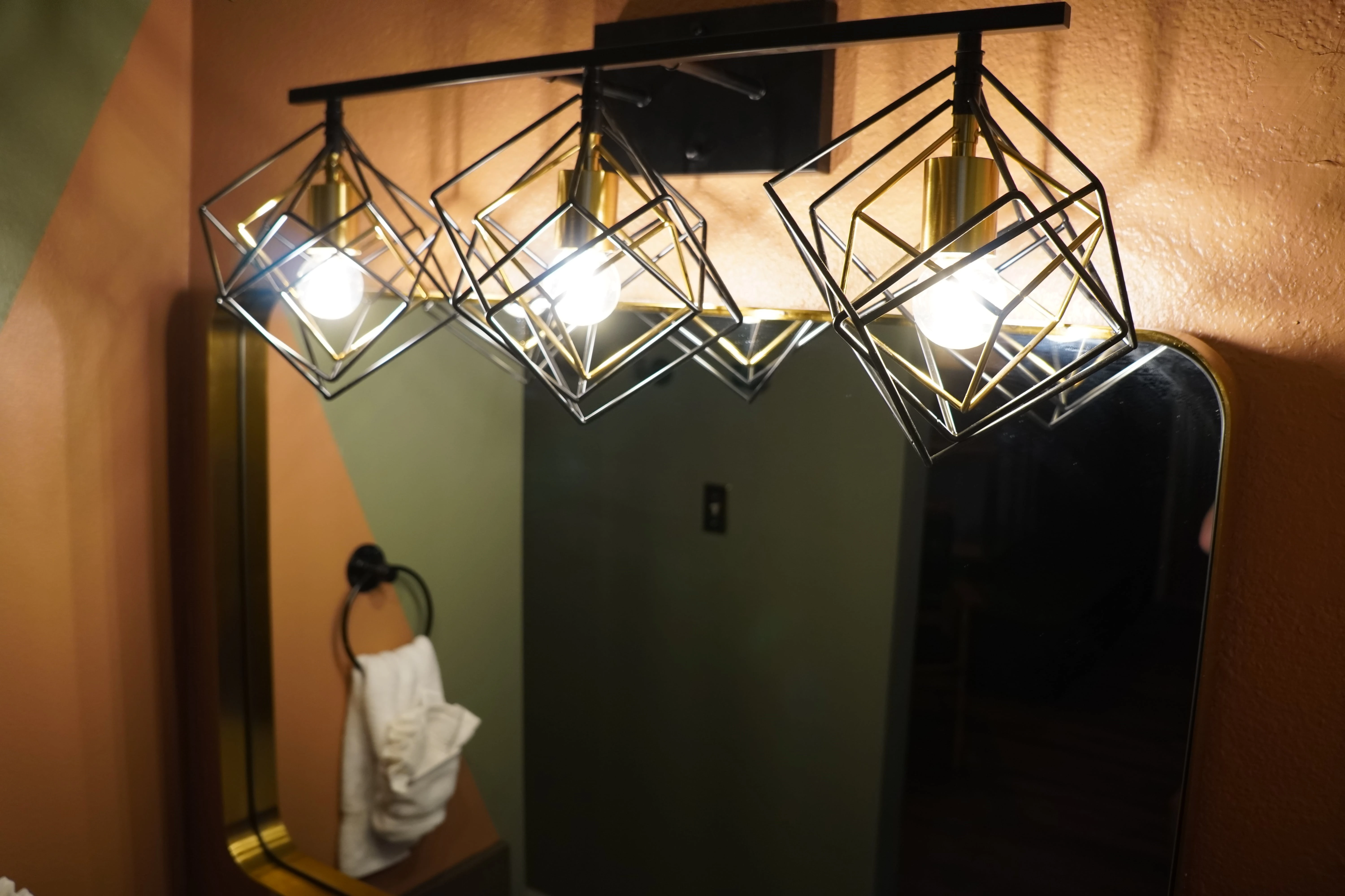 A close-up view of a light fixture above a mirror in a bathroom with peach and green walls.