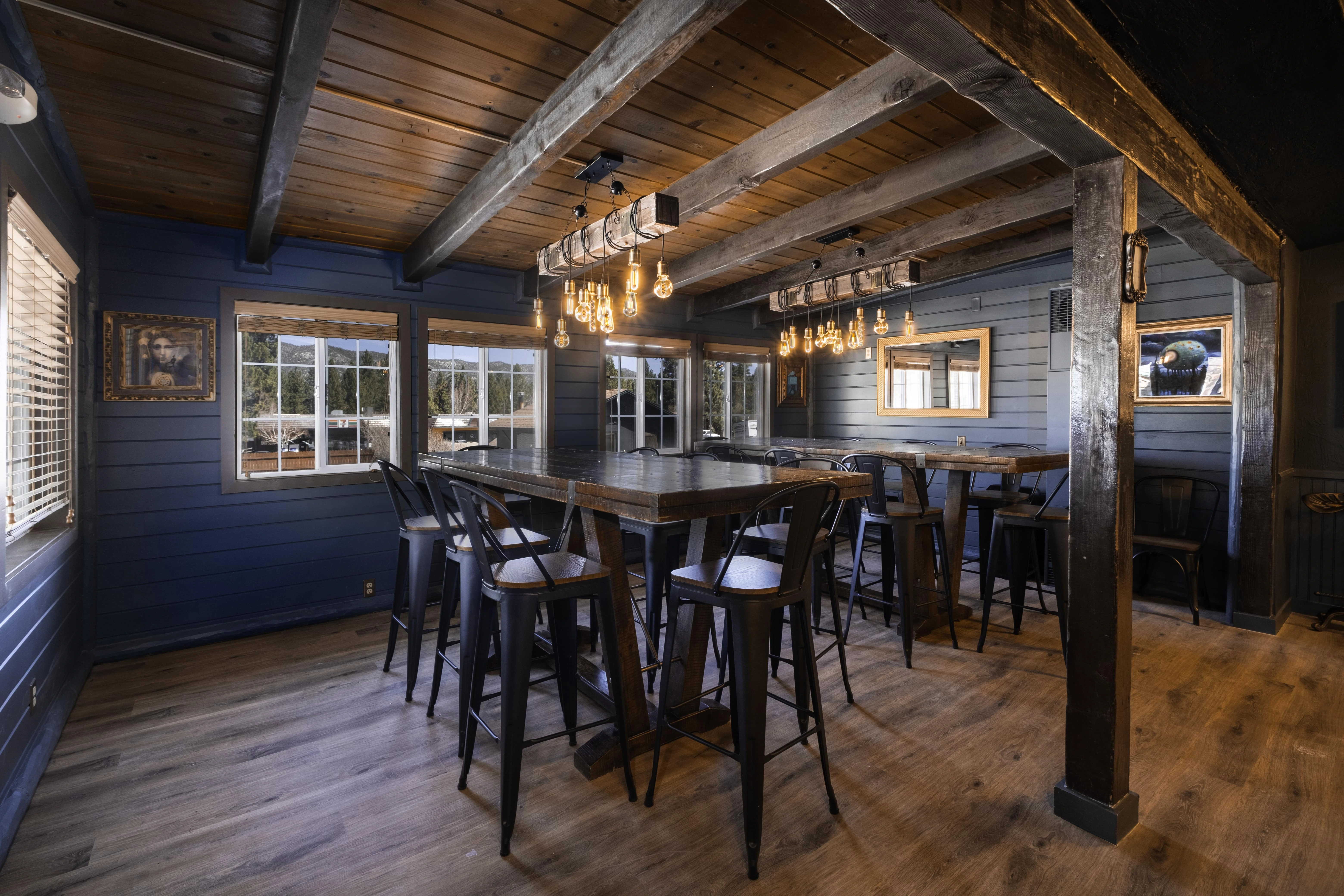 A large dining or lounge area with a high ceiling, wooden beams, and a large table with stools.