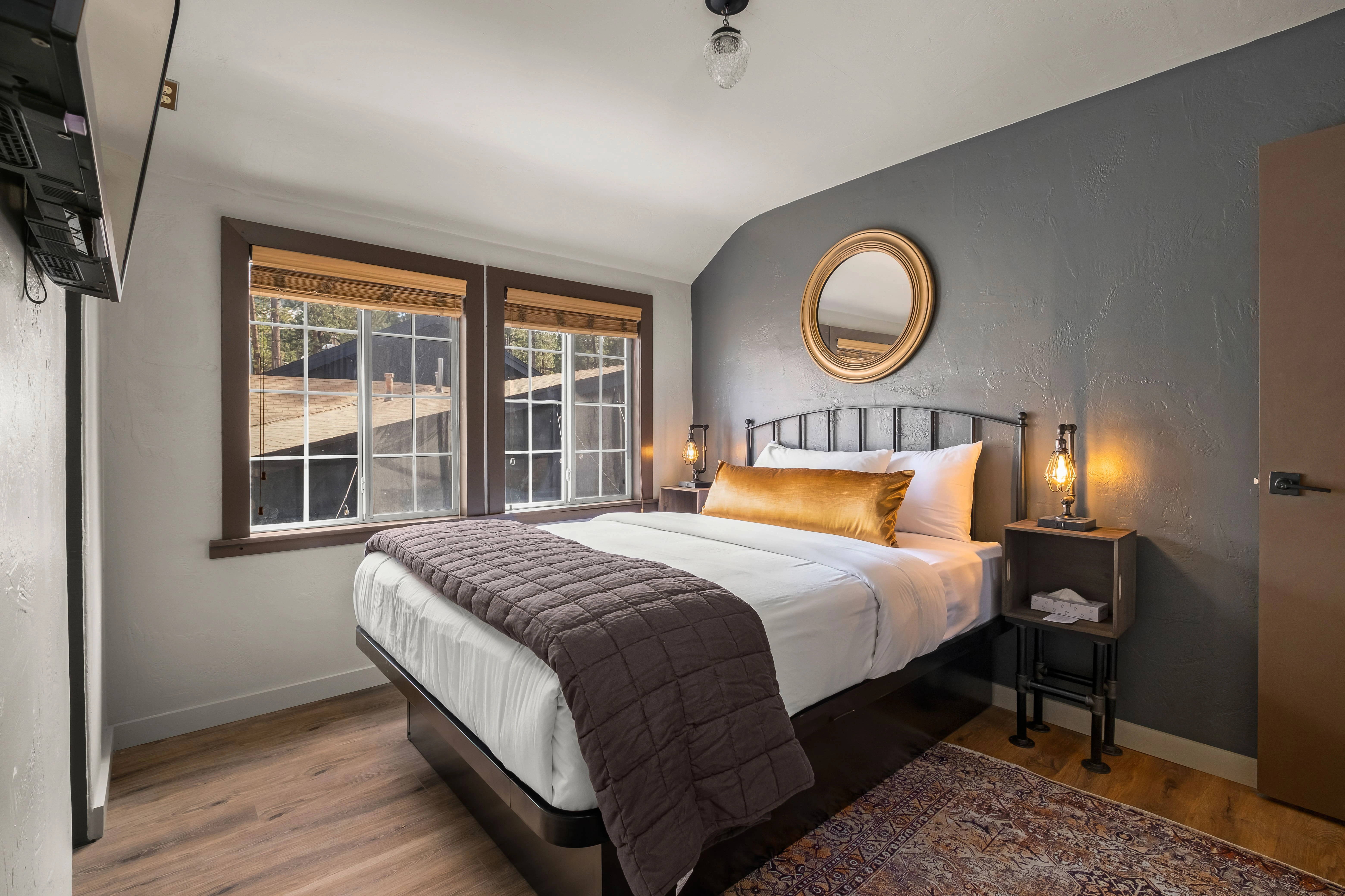 A hotel room with a bed, window, mirror, and nightstand