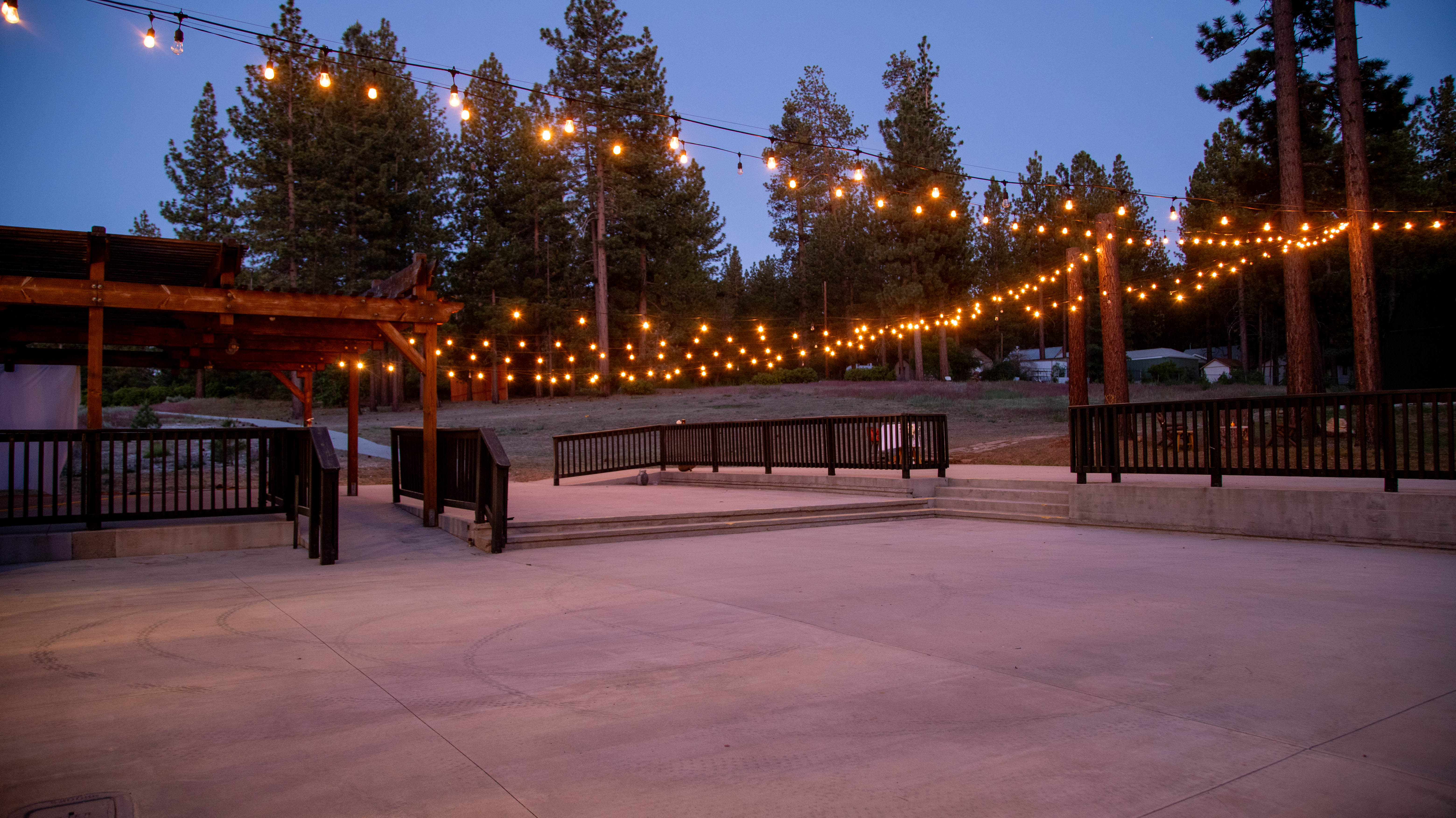 A lit outdoor patio area with string lights, wooden furniture, and trees in the background.
