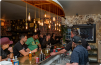 A blurry photo of a group of people sitting at a bar counter with a bartender serving drinks.