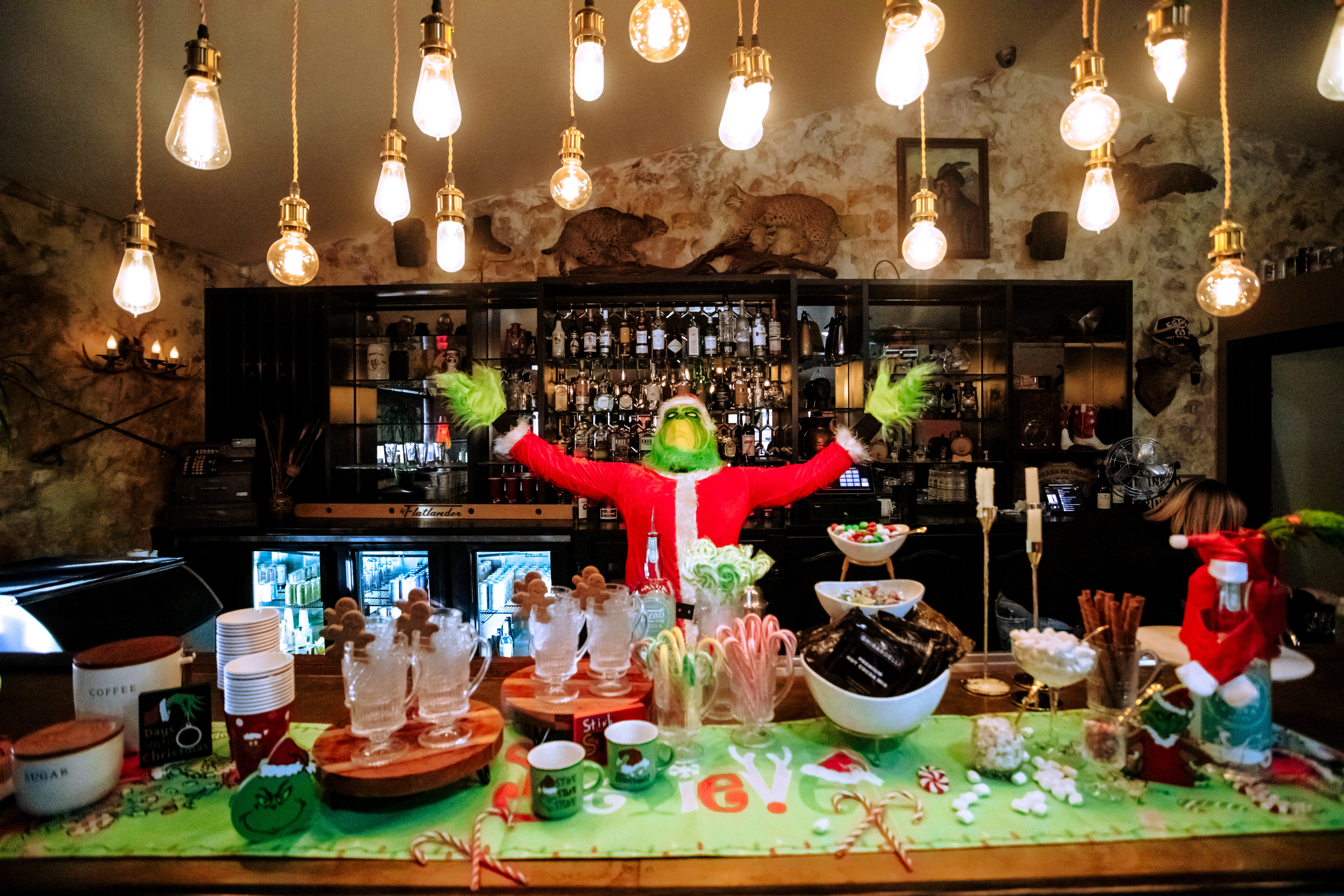 A bar decorated for Christmas with a Grinch doll, green runner, and festive decorations.