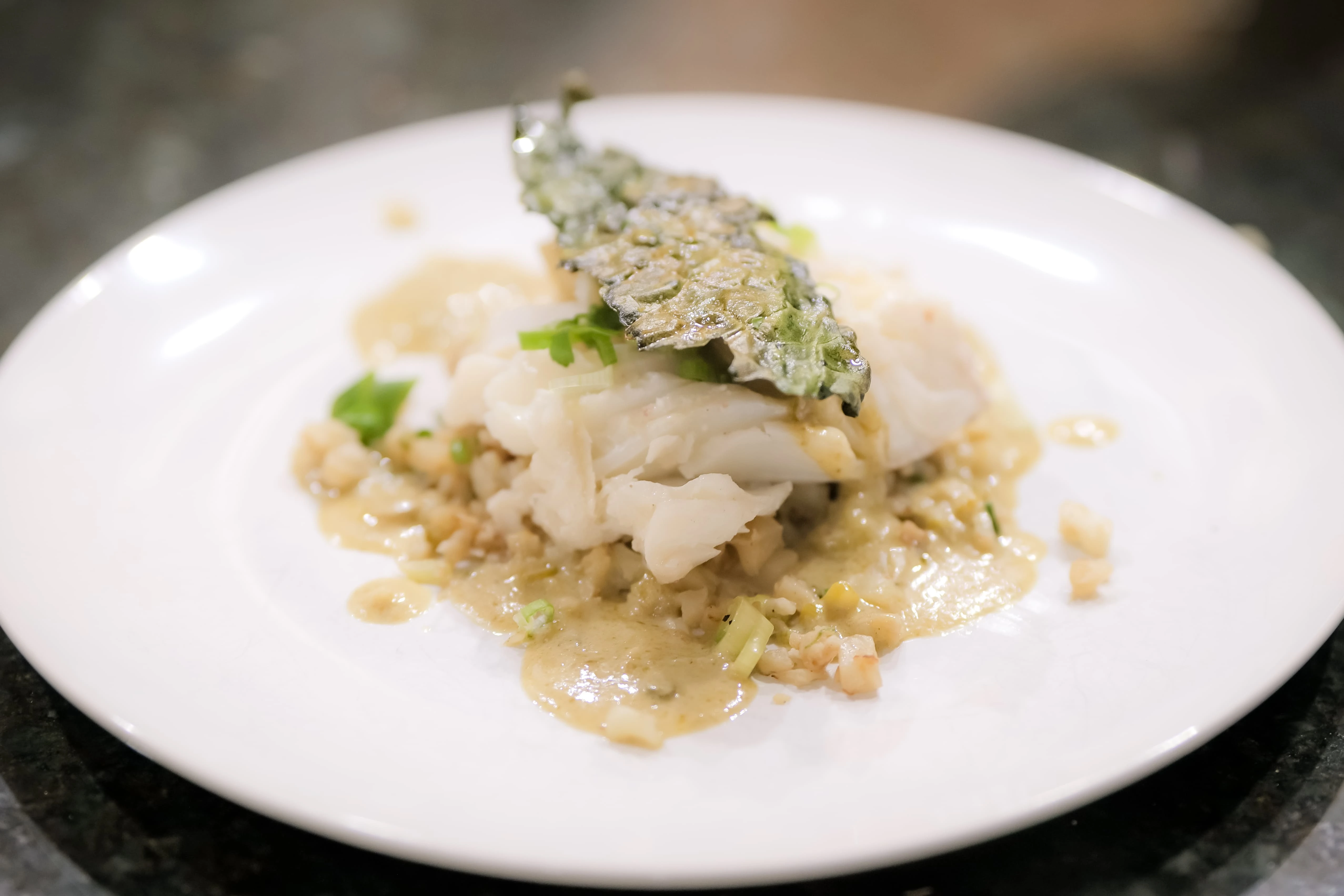 A plated fish dish with green herbs and sauce on a white plate.