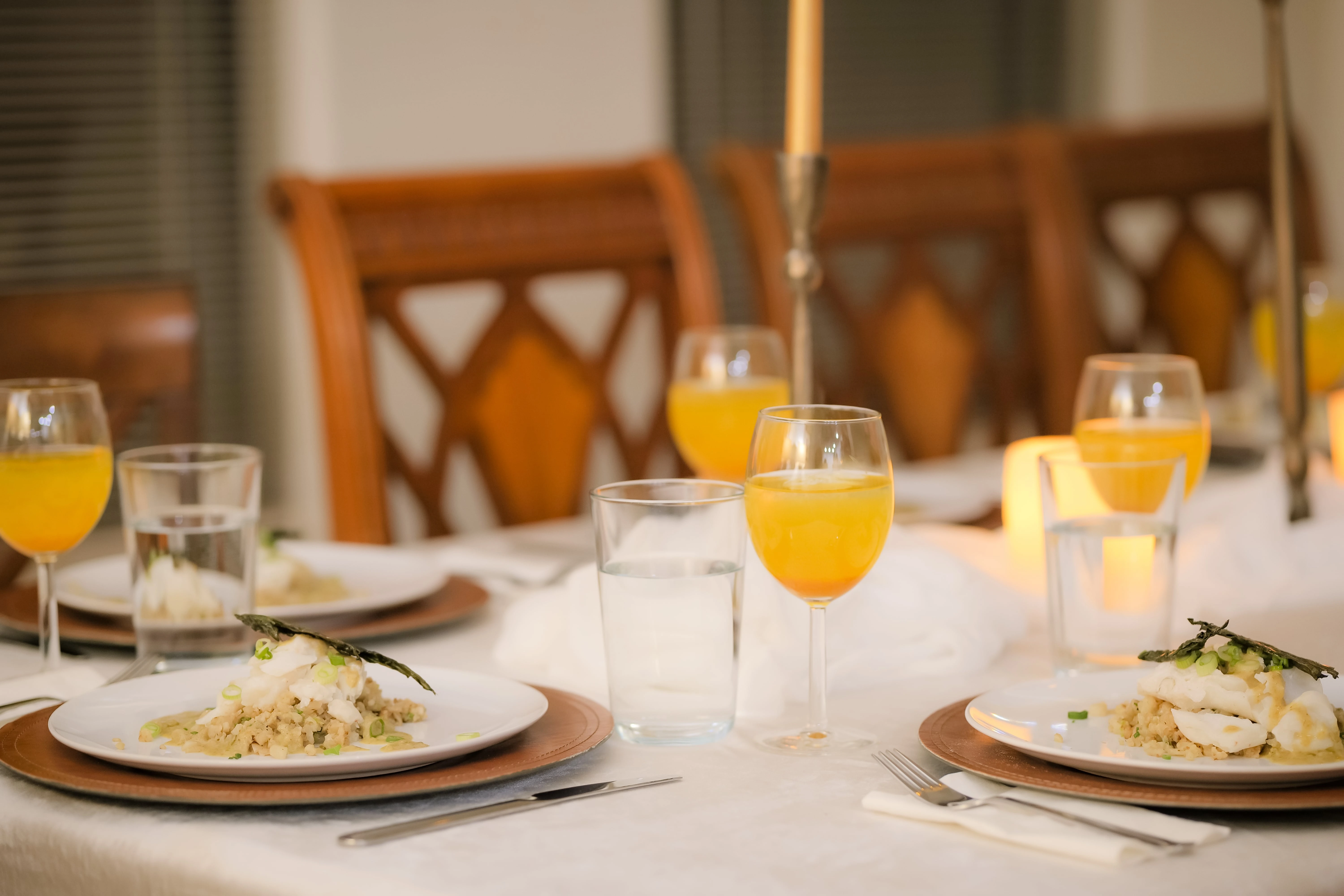 A table set for breakfast with plates of food, glasses of orange juice, and a candle